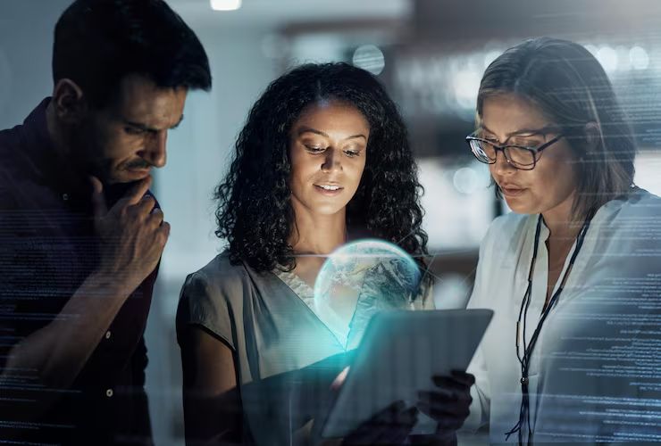 Three colleagues study a glowing globe projected from a tablet